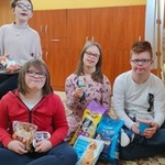 Grupa uczniów siedzi na dywanie. Przed sobą trzymają torby z karma dla zwierząt.