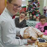 Uczeń trzyma talerz z ciastem w kształcie choinki. W tle stół wigilijny.