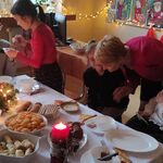 Uczniowie siedzą wokół stołu. Nauczycielka i uczennica łamią się opłatkiem.