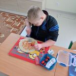 Uczeń siedzi przy stoliku i smaruje spód pizzy keczupem.
