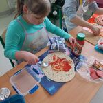 Uczennica siedzi przy stoliku i smaruje spód pizzy keczupem.