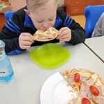 Uczeń siedzi przy stoliku i je kawałek pizzy. Przed nim stoi talerz z pizzą.