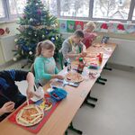 Uczniowie siedzą przy stolikach i przygotowują pizzę.