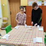 Uczennica i uczeń nakrywają stół, układają sztućce.