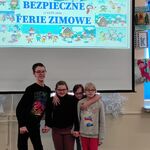 Czwórka uczniów stoi na tle ekranu z napisem Bezpieczne ferie zimowe.
