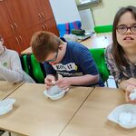 Uczniowie siedzą przy stolikach i robią kule ze śniegu znajdującego się w pojemnikach które stoją przed nimi.