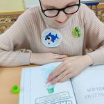 Uczennica siedzi przy stole i patrzy na kartę pracy w zeszycie.