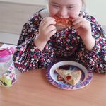 Uczennica siedzi przy stoliku i je pizzę.