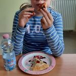 Uczennica siedzi przy stoliku i je pizzę.