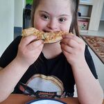 Uczennica siedzi przy stoliku i je pizzę.