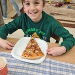 Uczeń siedzi przy stoliku. Przed nim na stole stoi talerz z kawałkiem pizzy.