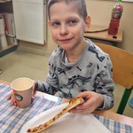 Uczeń siedzi przy stoliku i bierze kawałek pizzy z talerzyka.