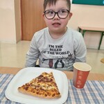 Uczeń siedzi przy stoliku. Przed nim na stole stoi talerz z kawałkiem pizzy i kubek z piciem.