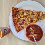 Talerzyk papierowy z pizzą, pojemnik z keczupem oraz kubek z piciem.