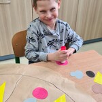 Uczeń przykleja element na papierową pizzę leżącą na stole.