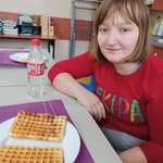 Uczennica siedzi przy stole. Przed nią stoi talerz z goframi.