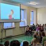 Uczniowie siedzą na ławeczkach i oglądają wyświetlany film.