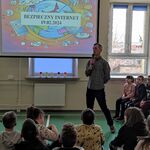 Uczniowie siedzą na ławeczkach i słuchają nauczyciela.
