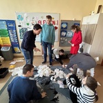 Uczniowie patrzą na kawałki papieru leżące na dywanie.