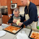 Uczeń kładzie plastry sera na spód pizzy posmarowany keczupem.