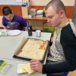 Uczeń kładzie plastry sera na spód pizzy posmarowany keczupem.