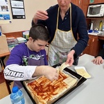Uczeń kładzie plastry sera na spód pizzy posmarowany keczupem.