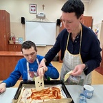Uczeń kładzie plastry sera na spód pizzy posmarowany keczupem.