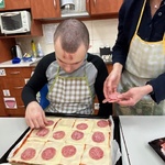 Uczeń z pomocą nauczyciela kładzie plastry salami na spód pizzy.