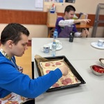 Uczeń kładzie plastry salami na spód pizzy.