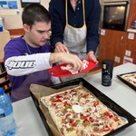 Uczeń kładzie pokrojone pieczarki na pizzę.