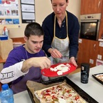 Uczeń kładzie kawałki sera na pizzę.