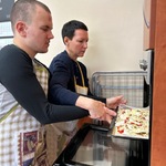 Uczeń z pomocą nauczyciela wstawia blachę z pizzą do piekarnika.