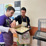 Uczeń z pomocą nauczyciela wstawia blachę z pizzą do piekarnika.