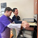 Uczeń z pomocą nauczyciela wstawia blachę z pizzą do piekarnika.