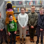 Uczniowie stoją obok osoby przebranej w strój dinozaura.