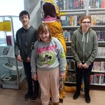 Uczniowie stoją obok osoby przebranej w strój dinozaura.