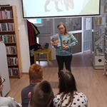 Uczestnicy zajęć w bibliotece słuchają pani bibliotekarki.