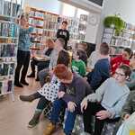 Uczestnicy zajęć w bibliotece słuchają pani bibliotekarki.