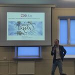 Uczniowie siedzą na ławeczkach i słuchają pana profesora omawiającego slajd wyświetlany na ekranie.