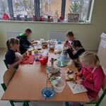 Uczniowie siedzą wokół stołu. przed nimi na stole leżą produkty spożywcze do przygotowania sałatki.