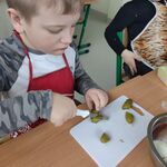 Uczeń siedzi przy stoliku i kroi ogórek.