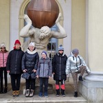 Uczniowie stoją na tle rzeźby Atlas . Uczniowie oglądają malowidła na ścianie.