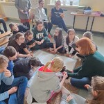 Uczniowie siedzą na dywanie, głaszczą królika.
