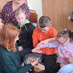 Uczniowie i nauczycielka przyglądają się jak uczennica głaszcze szynszyla.