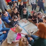 Uczniowie siedzą na dywanie, przed nimi kica królik.