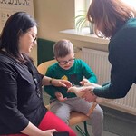 Uczeń siedzi na krześle, głaszcze kurę. Obok są dwie opiekunki