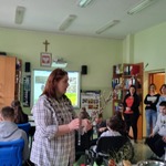 Edukatorka trzyma bazie w ręku. Wokół uczniowie uczestniczący w warsztatach.