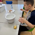 Uczeń siedzi przy stole. Przed nim stoi miska i jajka w kubku.