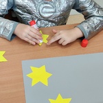 Uczeń w stroju kosmonauty smaruje klejem żółtą gwiazdkę.