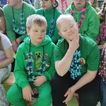 Grupa uczniów w kolorowych girlandach kwiatowych siedzi na ławce.